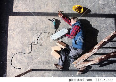 Male worker lying on the floor after fall from ladder, holding his knee. Work injury, accident in workplace. Male worker lying on the floor after fall from ladder, holding his knee. Work injury, accident in workplace. 114939822