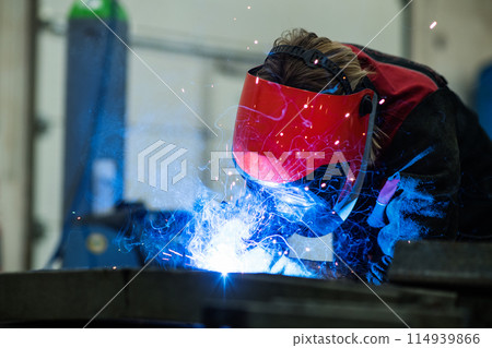 Close up of work of welder in workshop, operating welding machine, wearing protective clothing and a welding mask. Close up of work of welder in workshop, operating welding machine, wearing protective clothing and a welding mask. 114939866