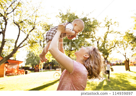 Mother holding baby boy in hands, playing with him. Low angle shot. Mother holding baby boy in hands, playing with him. Low angle shot. 114939897