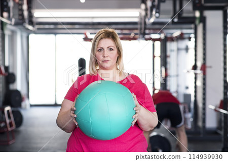Portrait of overweight woman exercising in gym, holding medicine ball Portrait of overweight woman exercising in gym, holding medicine ball 114939930