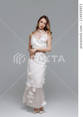 A woman in a white dress with flowers on it poses for a photo A woman in a white dress with flowers on it poses for a photo 114939953