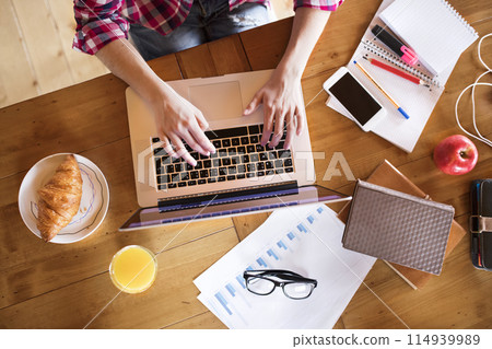 Top view on desk of university student is writing her thesis on a laptop, sitting at home on the couch. 114939989