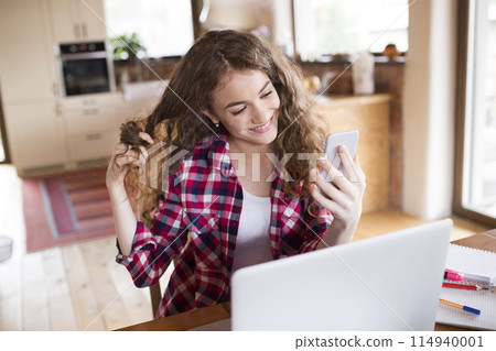 A beautiful university student is writing her thesis on a laptop, sitting at home on the couch. 114940001
