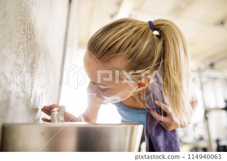 Beautiful sport woman drinking water afeter training in gym. Routine workout for woman's physical and mental health. 114940063