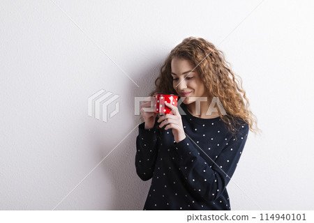 Portrait of a gorgeous teenage girl with curly hair drinking tea from mug. Studio shot, white background with copy space Portrait of a gorgeous teenage girl with curly hair drinking tea from mug. Studio shot, white background with copy space 114940101