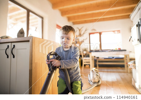 Young son helping mother with hosehold chores, vacuuming and cleaning their house. Weekly chores, weekend activities. Young son helping mother with hosehold chores, vacuuming and cleaning their house. Weekly chores, weekend activities. 114940161