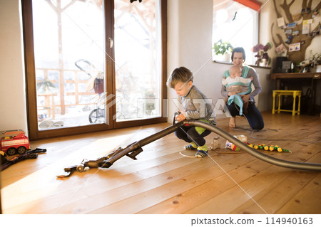 Young son helping mother with hosehold chores, vacuuming and cleaning their house. Weekly chores, weekend activities. Young son helping mother with hosehold chores, vacuuming and cleaning their house. Weekly chores, weekend activities. 114940163