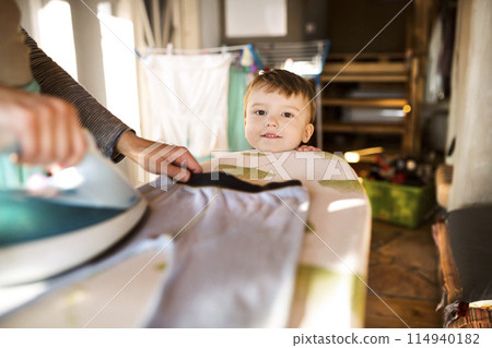 Son looking at mother ironing. Family doing household chores. 114940182