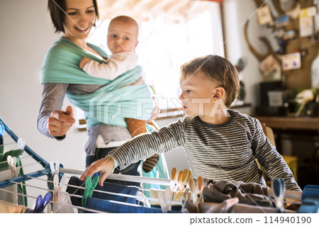 Young son helping mother with hosehold chores, hanging clothes on drying rack. Weekly chores, weekend activities. Young son helping mother with hosehold chores, hanging clothes on drying rack. Weekly chores, weekend activities. 114940190
