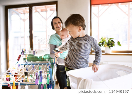 Young son helping mother with hosehold chores, hanging clothes on drying rack. Weekly chores, weekend activities. Young son helping mother with hosehold chores, hanging clothes on drying rack. Weekly chores, weekend activities. 114940197
