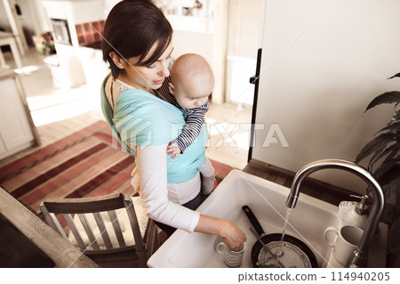 Mother holding small baby while cleaning dishes, carrying him around house in baby wrap. Household chores. Mother holding small baby while cleaning dishes, carrying him around house in baby wrap. Household chores. 114940205