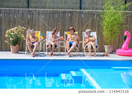 Group of cheerful seniors lying on lounge chairs by swimming pool and sunbathing. Spending hot day outdoors in backyard. Group of cheerful seniors lying on lounge chairs by swimming pool and sunbathing. Spending hot day outdoors in backyard. 114941526