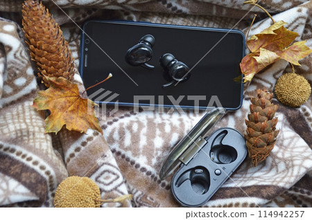 smartphone and wireless headphones on a background of pine cones and garland smartphone and wireless headphones on a background of pine cones and garland 114942257