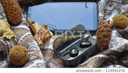 smartphone and wireless headphones on a background of pine cones and garland smartphone and wireless headphones on a background of pine cones and garland 114942258