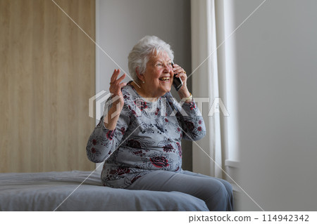 Senior woman at home, phone calling, sitting on bed. Older woman living alone, enjoying peaceful weekend day. 114942342