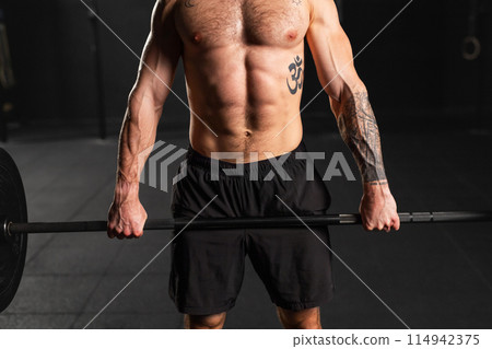 Strong man preparing for barbell lift, overhead squat, standing by barbell. Routine workout for physical and mental health. 114942375