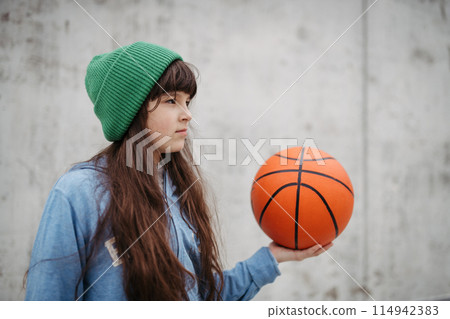 Sad girl alone in the city, want to play basketball. Young girl spending free time alone in the city, no friends, holding basketball. Sad girl alone in the city, want to play basketball. Young girl spending free time alone in the city, no friends, holding basketball. 114942383