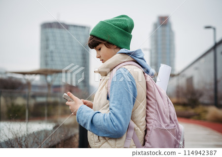 Girl standing in front of school building, scrolling on tablet. Using social media. Online bullying or cyberbullying for young schoolgirl. 114942387