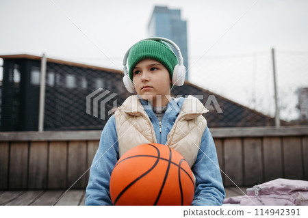 Sad girl alone in the city, want to play basketball. Young girl spending free time alone in the city, no friends, holding basketball. 114942391