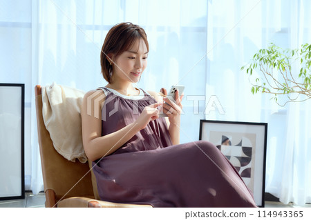 A woman sitting on a chair in a room and looking at her smartphone 114943365