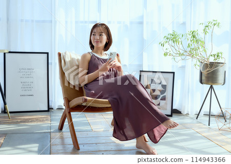 A woman sitting on a chair in a room and looking at her smartphone 114943366