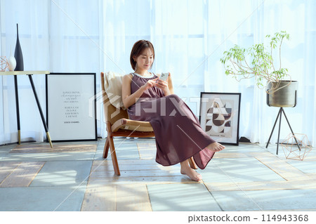 A woman sitting on a chair in a room and looking at her smartphone 114943368
