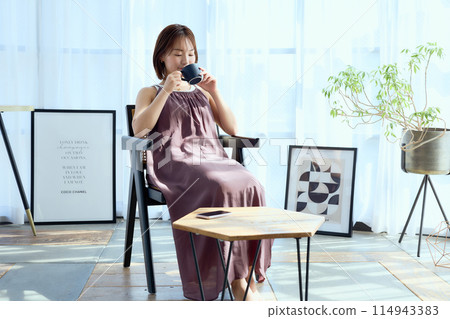 A woman sitting on a chair in a room and drinking coffee A woman sitting on a chair in a room and drinking coffee 114943383