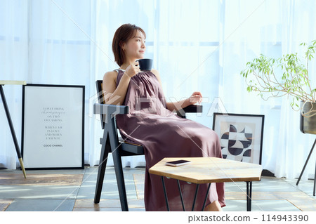 A woman sitting on a chair in a room and drinking coffee 114943390