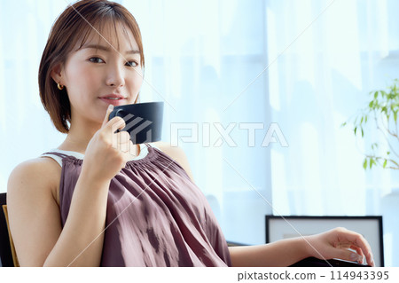 坐在房間椅上喝咖啡的女人 114943395