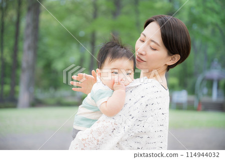A mother holding her baby in a park with fresh green leaves - an image of happiness, well-being, and motherly care A mother holding her baby in a park with fresh green leaves - an image of happiness, well-being, and motherly care 114944032