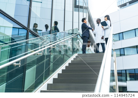 Businessmen and multinational researchers in white coats shaking hands in an office 114945724