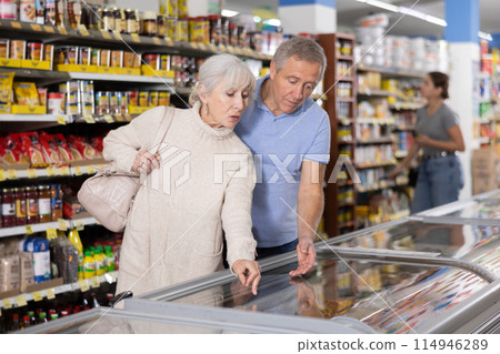 Man and woman purchasers choosing frozen product in supermarket Man and woman purchasers choosing frozen product in supermarket 114946289