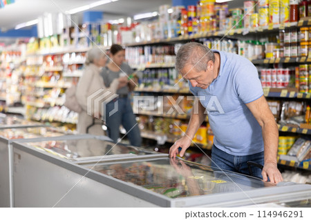 Mature man shopping in supermarket, choosing frozen convenience food 114946291