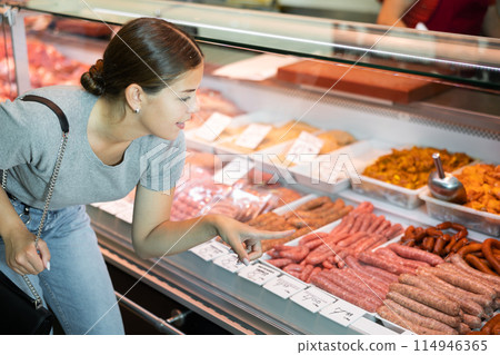 Young woman buyer chooses sausages in butcher shop Young woman buyer chooses sausages in butcher shop 114946365