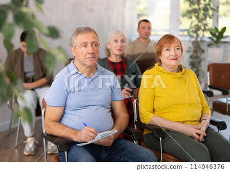 Interested aged man and woman listening to lecture in auditorium 114946376