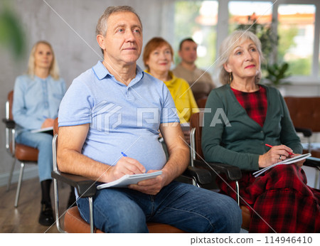 Motivated older man listening to lecture in auditorium with group 114946410