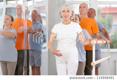 Active mature woman practicing first position holding by ballet barre together with others 114946491