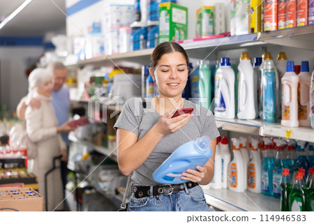 Woman purchaser taking photo of liquid detergent in big supermarket Woman purchaser taking photo of liquid detergent in big supermarket 114946583