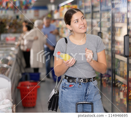 Young woman purchaser choosing cool drink in big supermarket 114946695