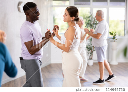 Girl teacher dances pair dance with african male student of fitness class Girl teacher dances pair dance with african male student of fitness class 114946730