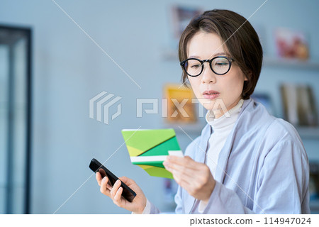 A woman looking at her bank account passbook with a troubled expression A woman looking at her bank account passbook with a troubled expression 114947024