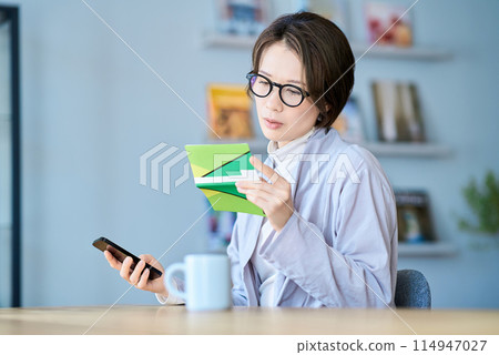 A woman looking at her bank account passbook with a troubled expression 114947027