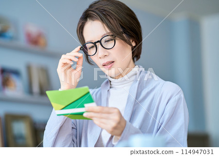 A woman looking at her bank account passbook with a troubled expression A woman looking at her bank account passbook with a troubled expression 114947031