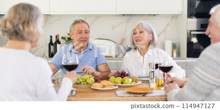 Two mature married couples are sitting at table, enjoying food and wine, chatting. Two mature married couples are sitting at table, enjoying food and wine, chatting. 114947127
