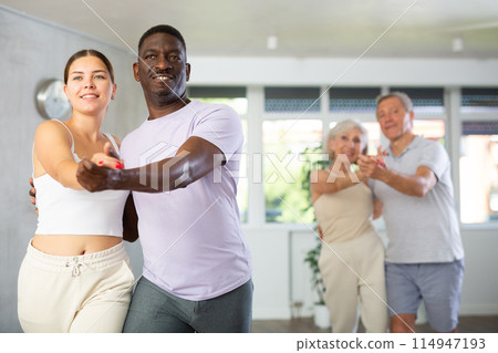 Young woman teaching group of multiethnic mature people social dance 114947193