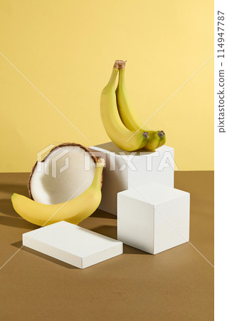 Many white empty platforms with different shapes are neatly arranged on a brown countertop, the same color as dried coconuts, and a yellow background, the same color as bananas. Space for displaying 114947787