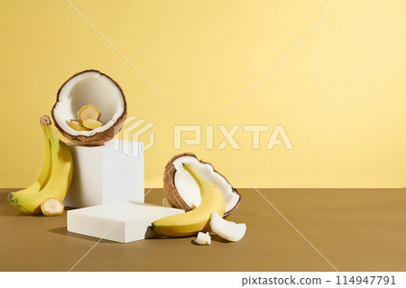 In the right corner of the photo are a few white display platforms placed next to each other, coconuts and bananas scattered around. The photo has yellow background and space for showing product 114947791