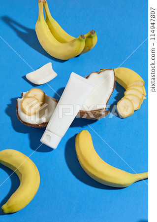 A unique template photo for the design with an overhead view at the blue tabletop with bananas and coconuts scattered arranged above, in the middle is a blank label tube for adding brand packaging 114947807