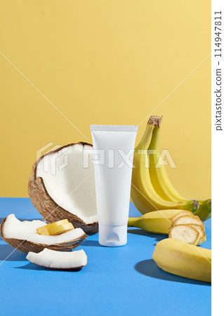 Vertical frame advertising photograph for beauty care products which extracted from natural fruits in tropical style with yellow-blue tones, an unlabeled tube surround by banana and coconut Vertical frame advertising photograph for beauty care products which extracted from natural fruits in tropical style with yellow-blue tones, an unlabeled tube surround by banana and coconut 114947811