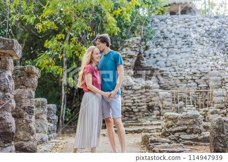 Couple, man and woman tourists at Coba, Mexico. Honeymoon Ancient mayan city in Mexico. Coba is an archaeological area and a famous landmark of Yucatan Peninsula. Cloudy sky over a pyramid in Mexico 114947939
